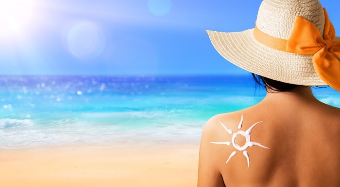 spate femeie la plaja cu palarie pe cap si cu lotiune aplicata in forma de soare pe piele