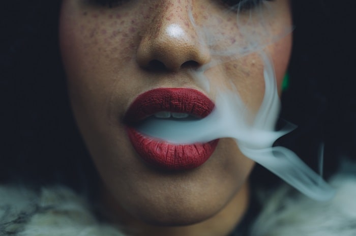detaliu fata de femeie cu fum de tigara care iese din gura