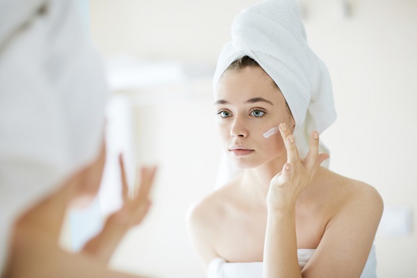 femeie in oglinda aplica crema cosmetica pe ten