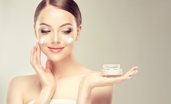 portret femeie cu un borcan de crema cosmetica in mana si crema aplicata pe ten