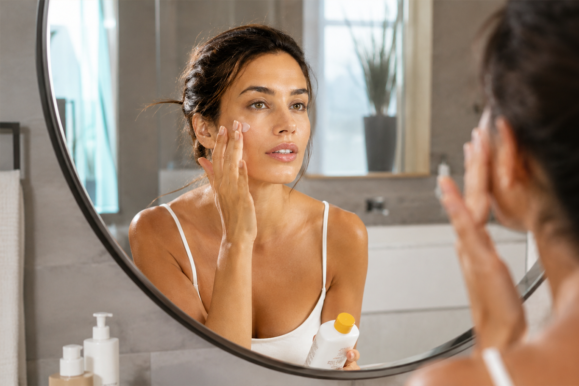 femeie care aplica spf 50 pe ten in oglinda