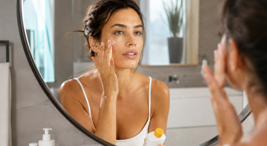 femeie care aplica spf 50 pe ten in oglinda
